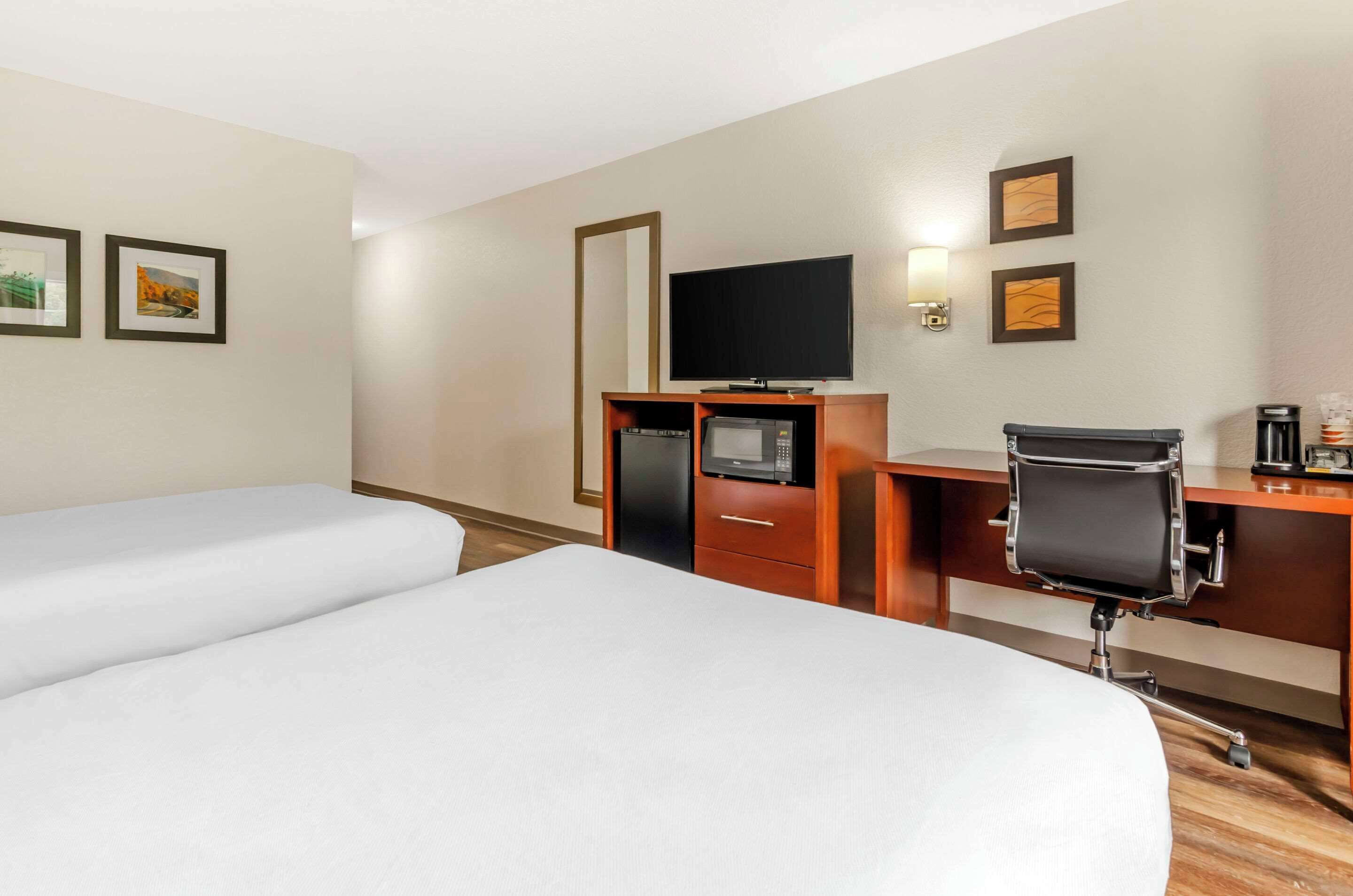 A hotel room with two beds, a desk with a chair, a TV, a microwave, and a coffee maker.