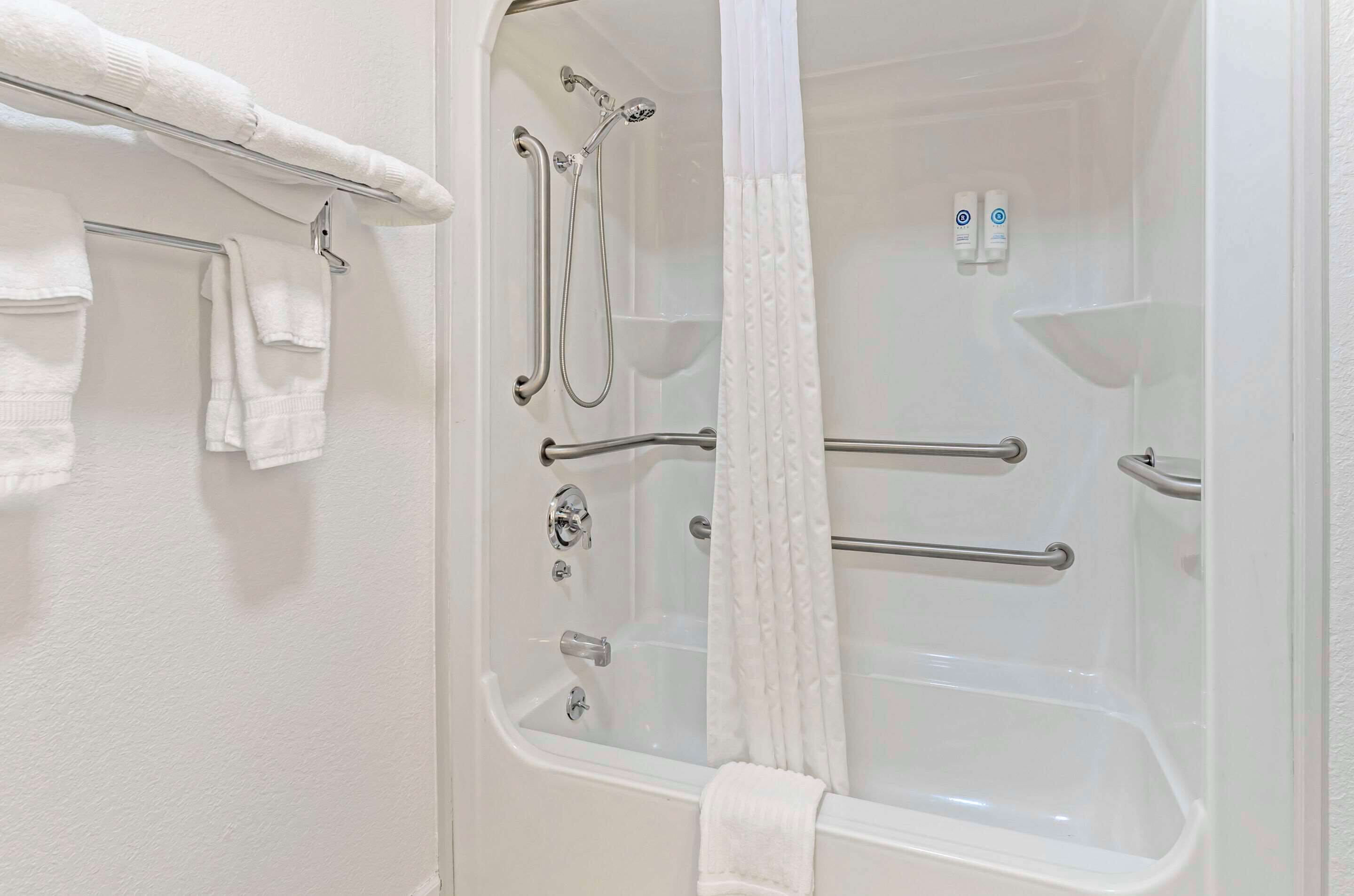 A bathroom with a bathtub, shower, and handrails.