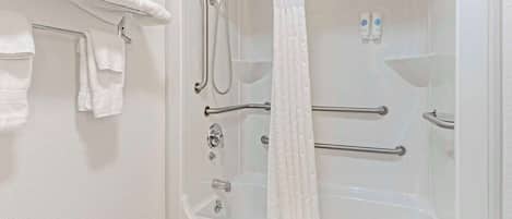 A bathroom with a bathtub, shower, and handrails.