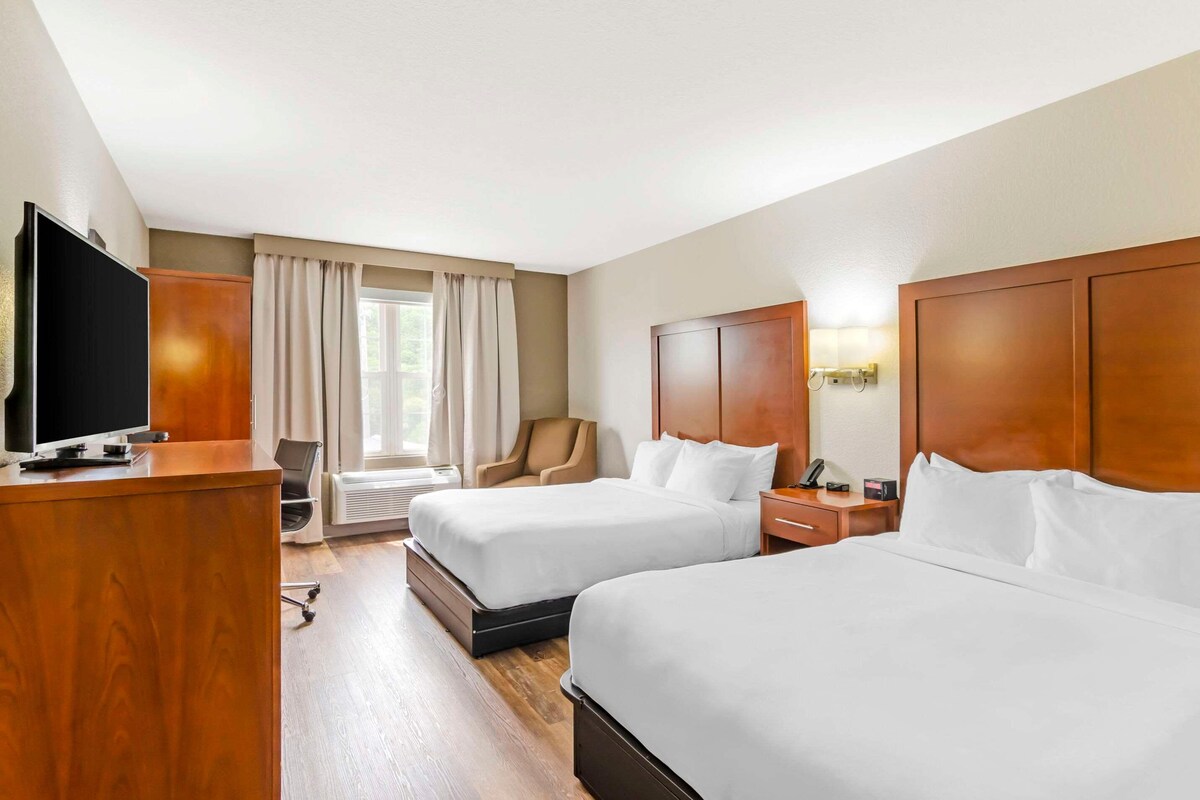 Habitación de hotel con dos camas, un escritorio, un televisor, una silla y una ventana con cortinas.
