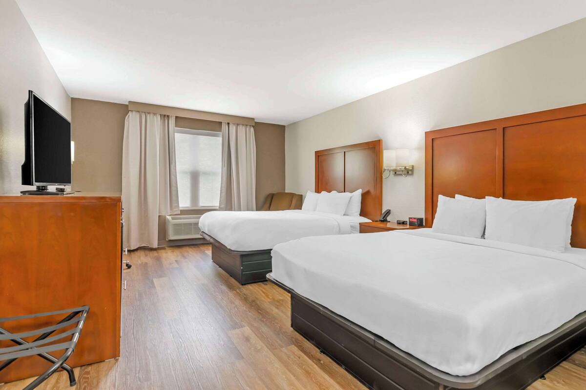 A hotel room with two beds, a TV, a desk, and a window with curtains.