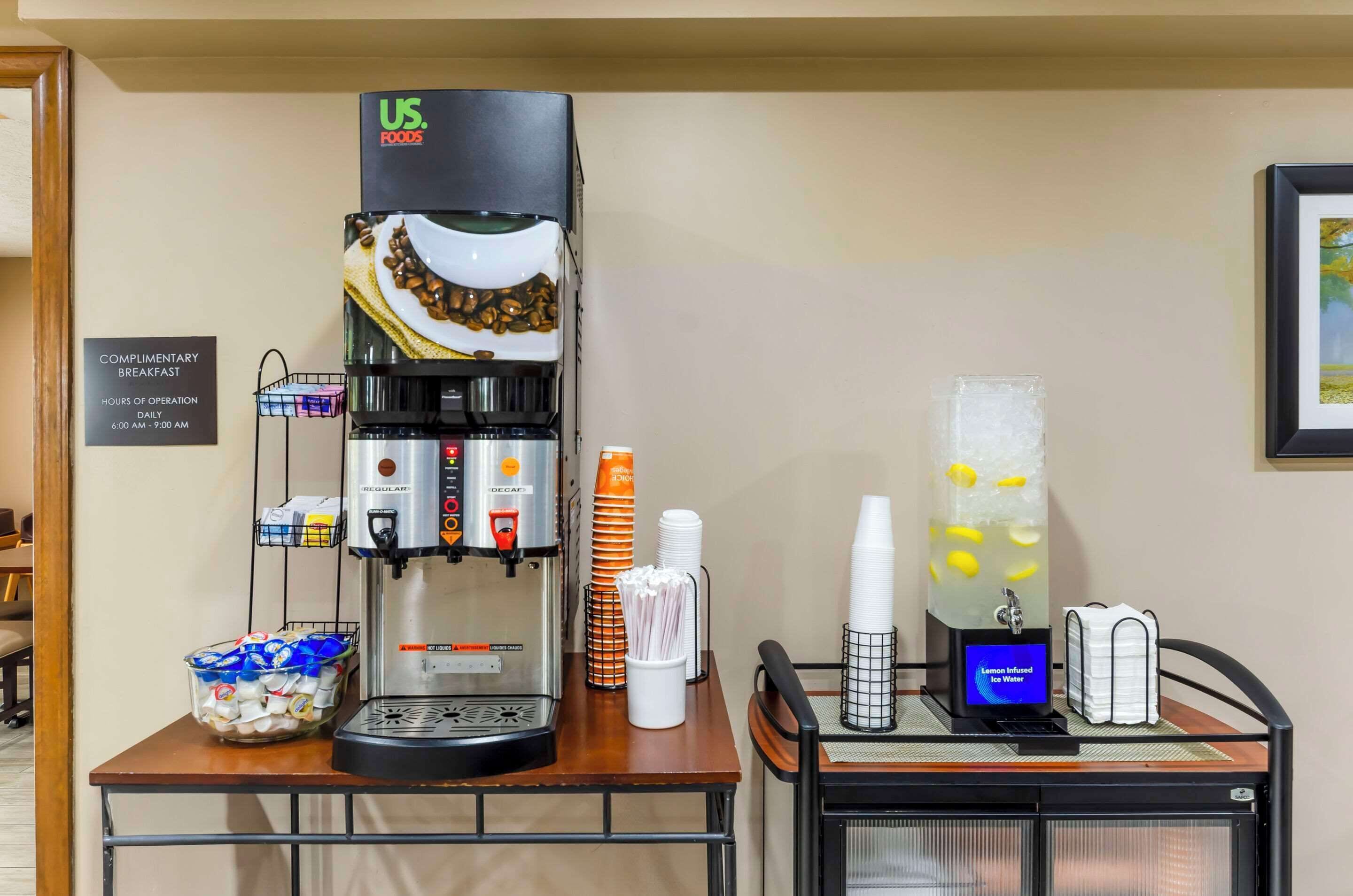 Een koffiehoek met een koffieapparaat van US Foods, een bordje met ‘complimentair ontbijt’ en een ijskoude waterdispenser met citroensmaak.