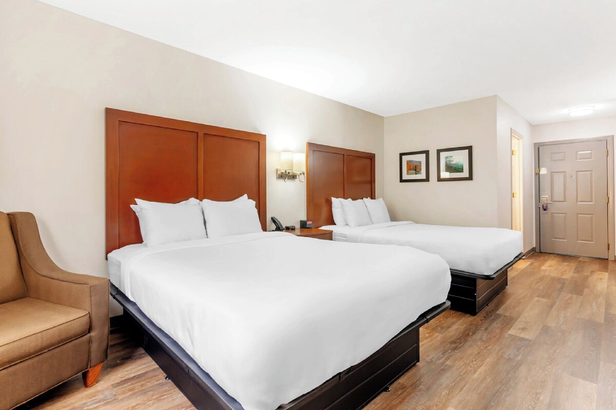 A hotel room with two beds, a sofa, a nightstand, and a door.
