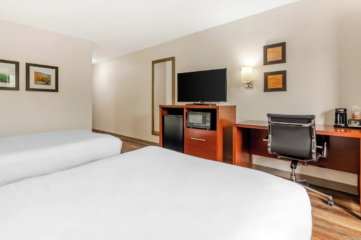 A hotel room with two beds, a desk, a chair, a television, a microwave, and a coffee maker.