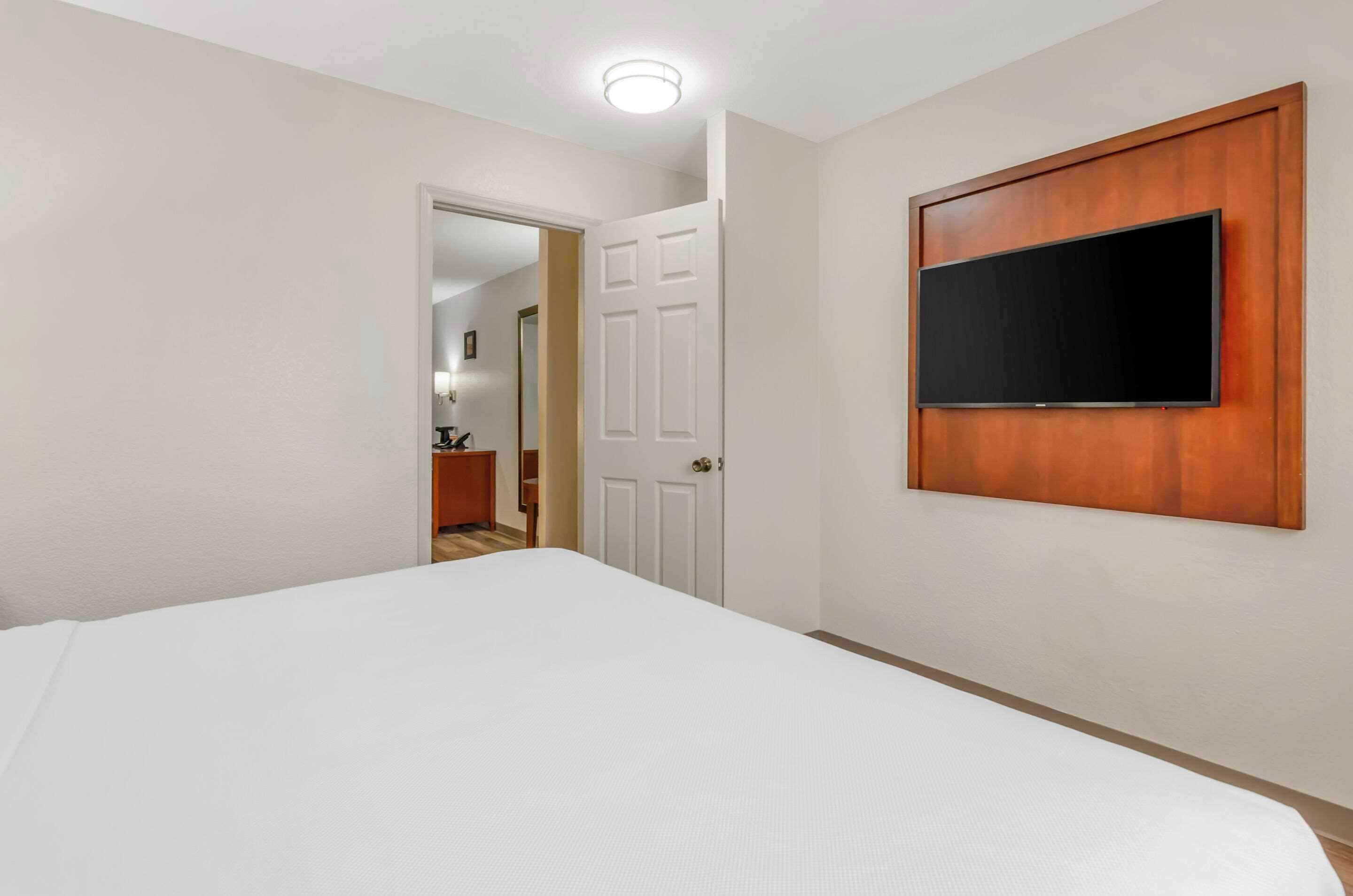 Un dormitorio con una cama, un televisor montado en la pared y una puerta que da a otra habitación.