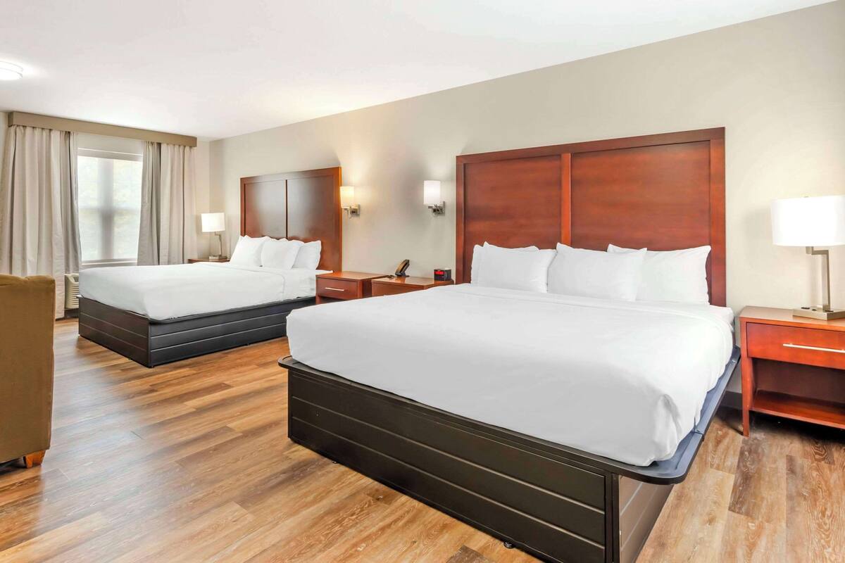 A hotel room with two beds, wooden headboards, a wooden floor, and a nightstand with a lamp.