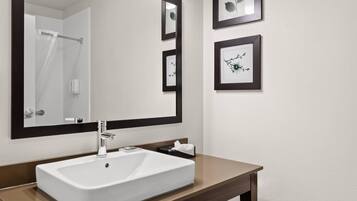 Un baño con un lavamanos blanco, un espejo grande y obras de arte enmarcadas en la pared.