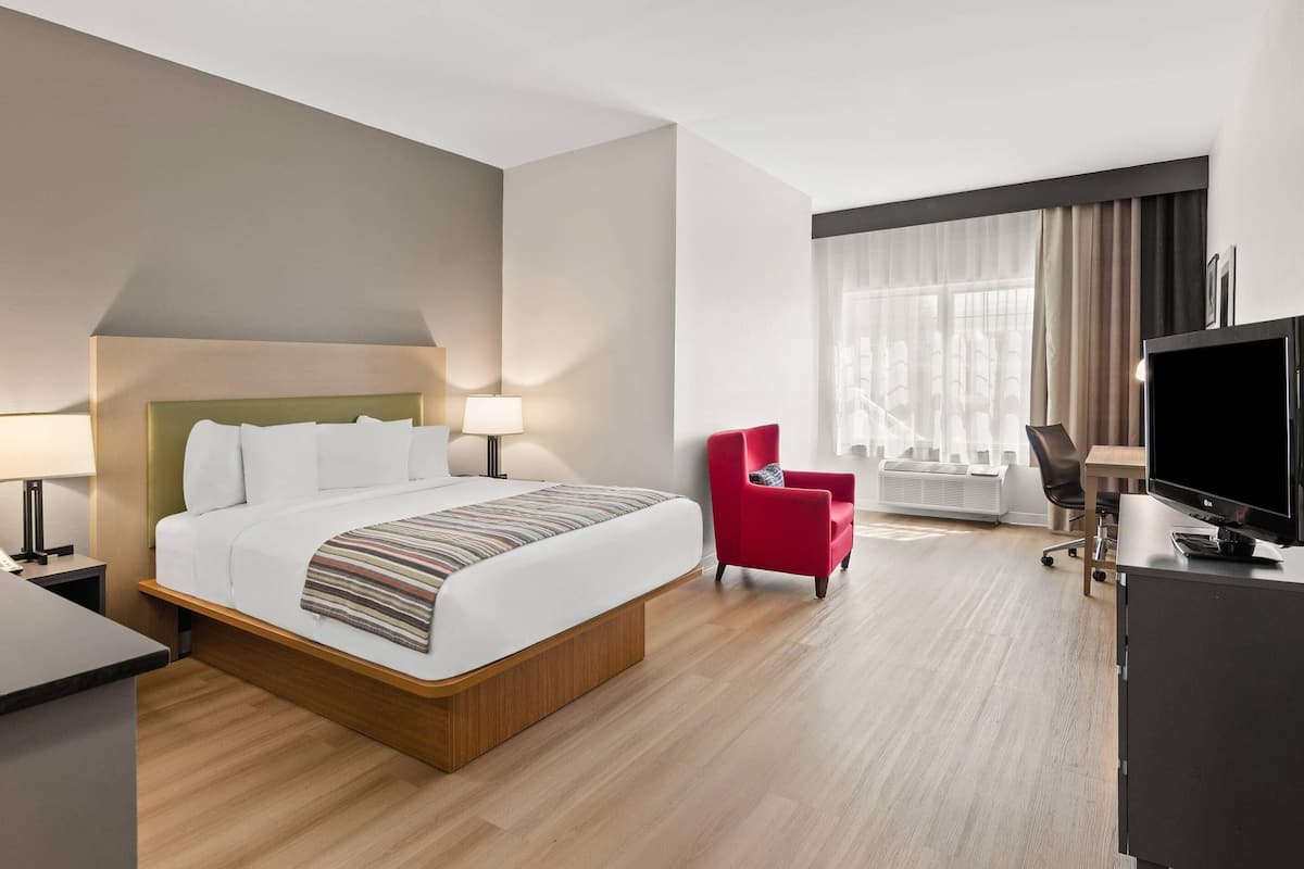 A hotel room with a bed, a desk, a chair, a TV, and a window with curtains.