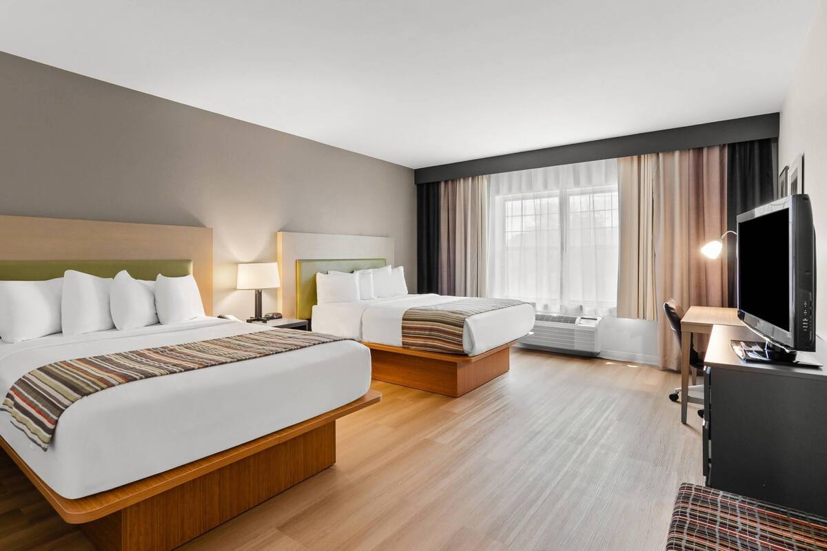A hotel room with two beds, a desk, a TV, and a window with curtains.