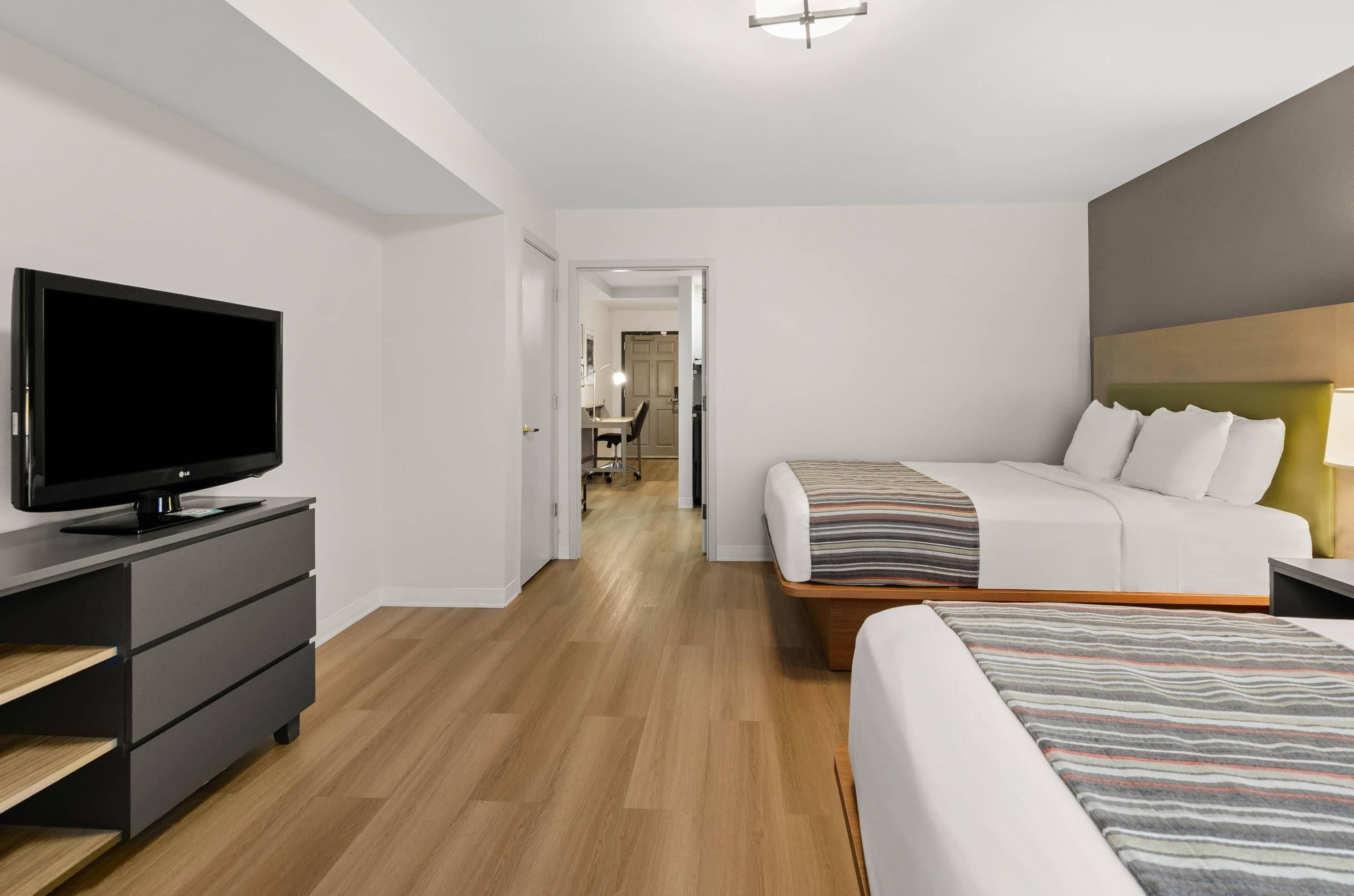 A modern hotel room with a flat-screen TV, a bed with a striped blanket, a bedside table, and a wooden floor.