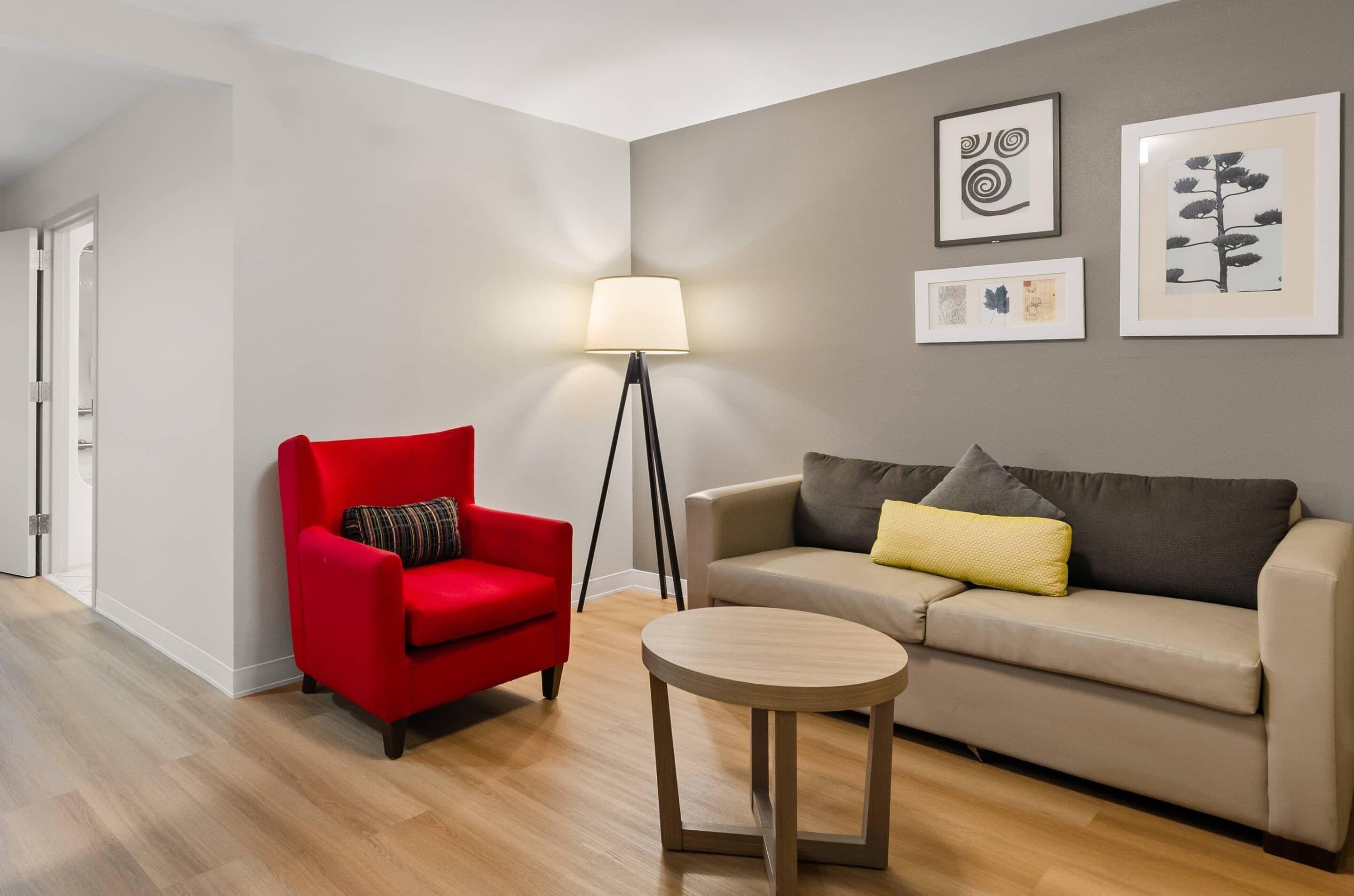 Ein modernes Wohnzimmer mit einem roten Sessel, einem beigen Sofa, einem kleinen runden Tisch und einer Stehlampe.