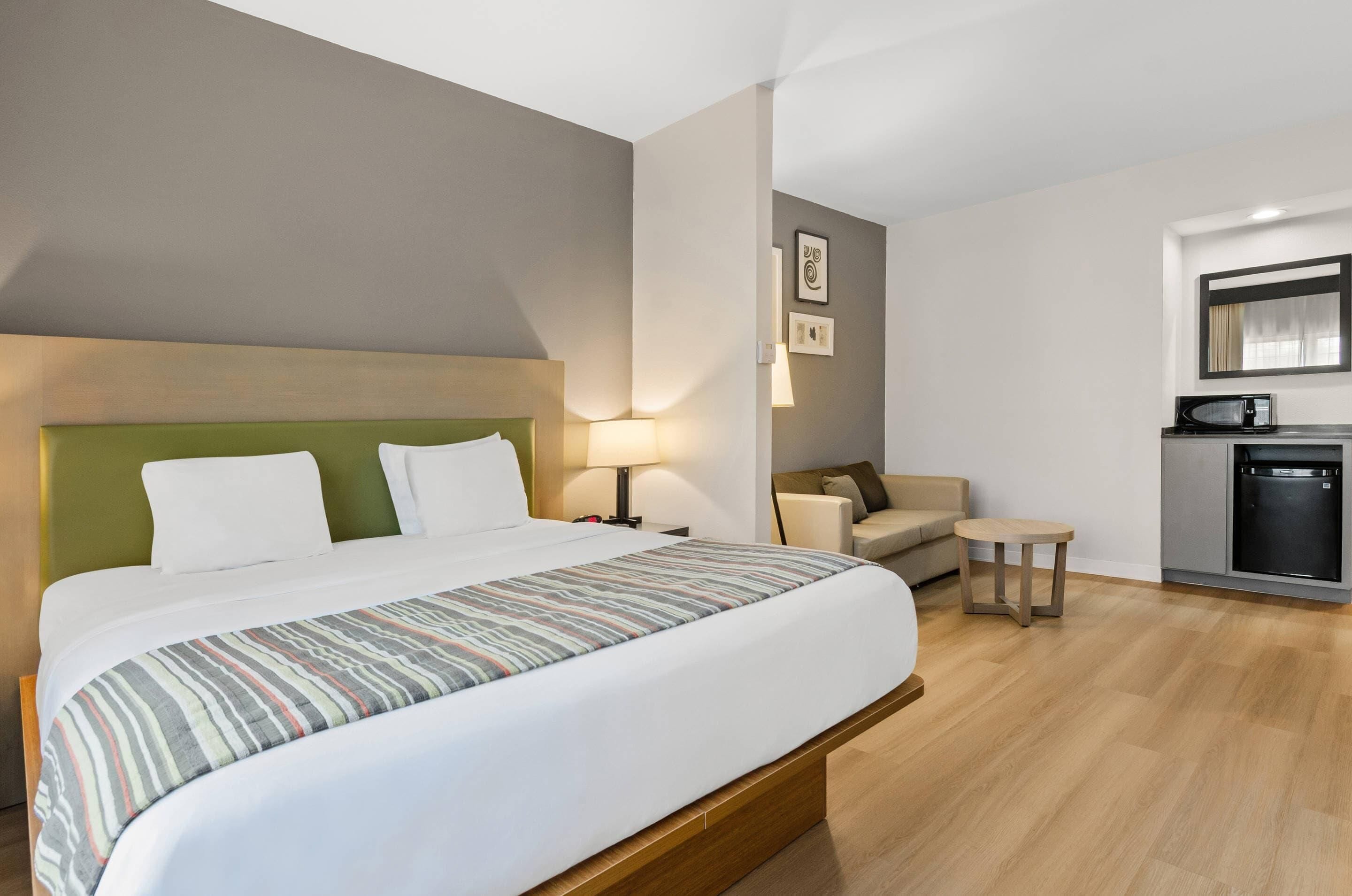 Une chambre d’hôtel avec un grand lit, un petit canapé, une table, un four à micro-ondes et un réfrigérateur.