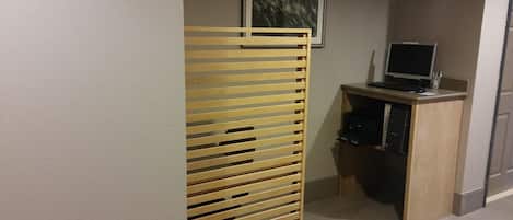 Un pasillo con un separador de listones de madera, un escritorio con una computadora y un cuadro en la pared.