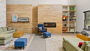 A modern living room with a wooden wall, a sofa, a chair, a coffee table, and a bookshelf. - Country Inn & Suites by Radisson, Roanoke, VA (Roanoke)