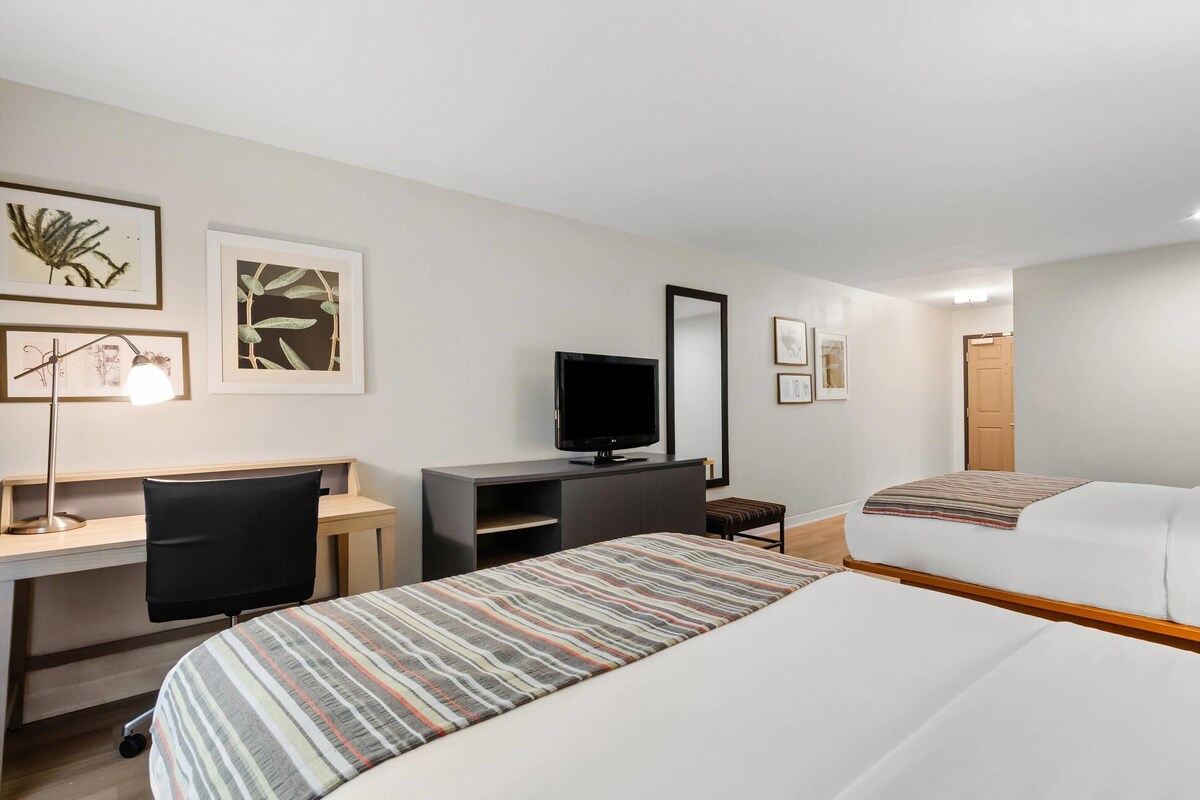 A hotel room with a bed, a desk with a chair, a television, and artwork on the walls.