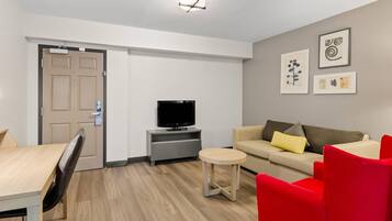 A modern living room with a TV, sofa, red chair, and artwork on the wall.