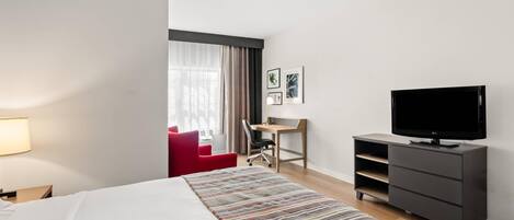 A hotel room with a bed, a desk, a chair, a television, and a red armchair.