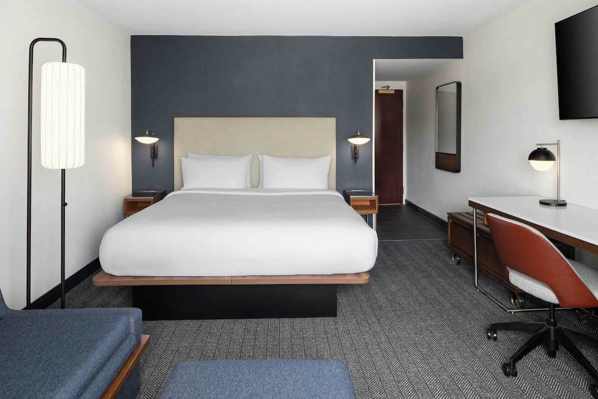 Una habitación de hotel con una cama grande, un escritorio, una silla, una lámpara y un espejo.
