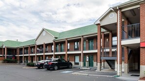Um motel de vários andares com fachada de tijolo, telhado verde e estacionamento com vários carros.
