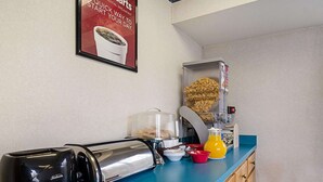 Uma cozinha compacta com torradeira, cafeteira, dispensador de cereais e jarra de frutas em uma bancada azul.