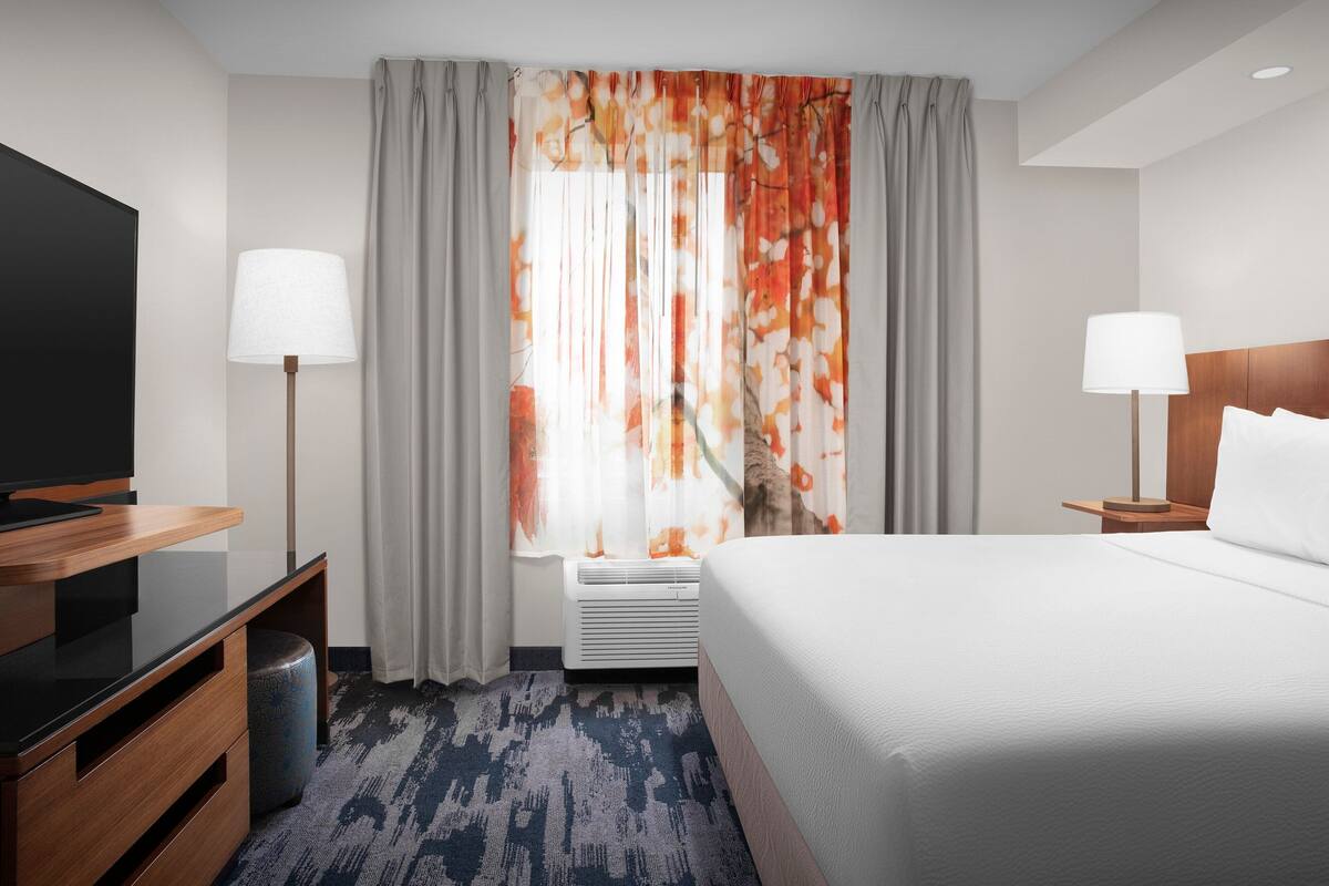 Een hotelkamer met een bed, een televisie, een bureau, een lamp en een raam met gordijnen.