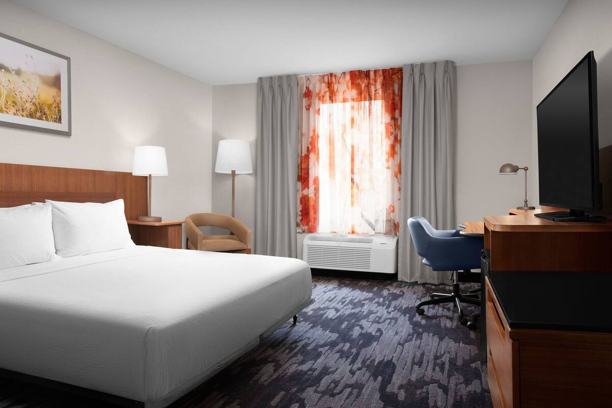Hotelkamer met een groot bed, een bureau, een stoel, een televisie en een raam met gordijnen.