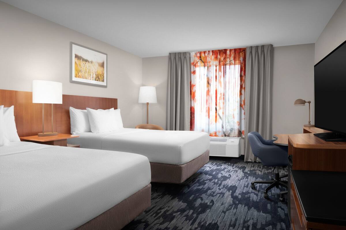 Een hotelkamer met twee bedden, een bureau, een stoel, een televisie en een raam met gordijnen.