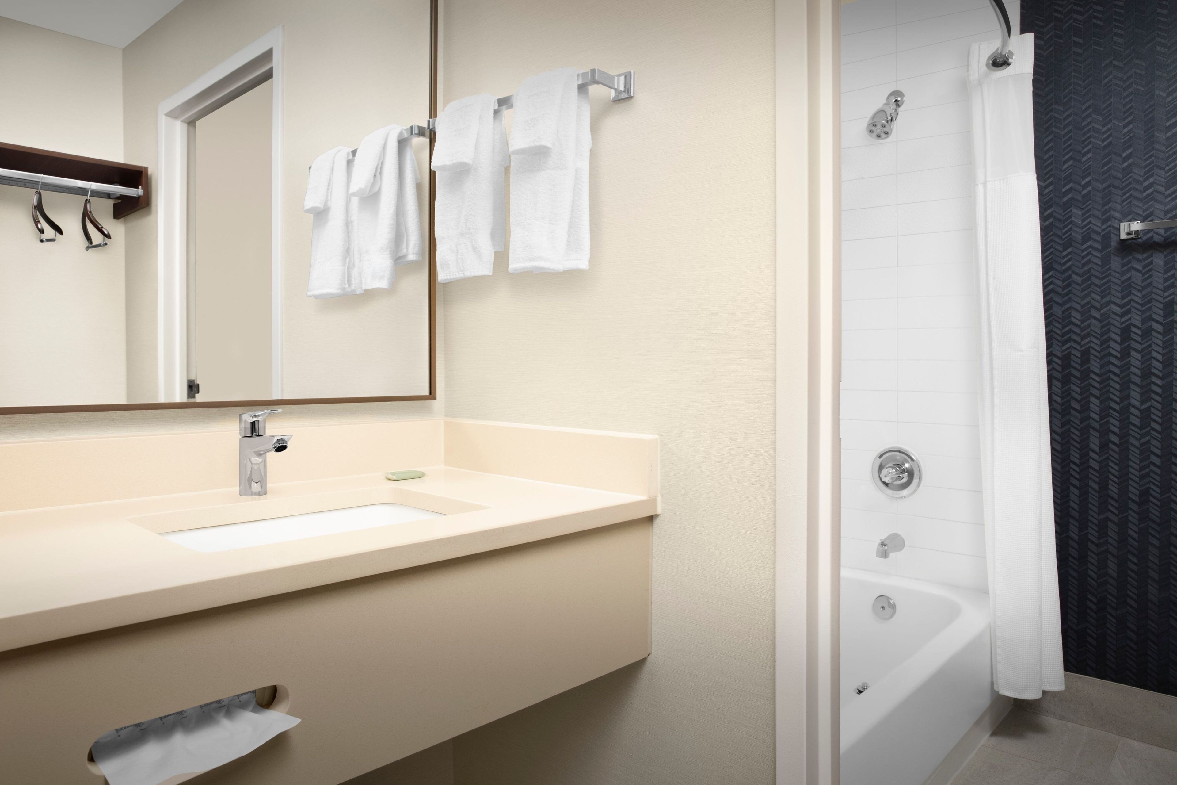 A bathroom with a sink, mirror, towel rack, and a shower area.