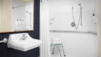 Un baño moderno con un lavamanos blanco, una ducha con cabezal de ducha manual y un mamparo de vidrio.
