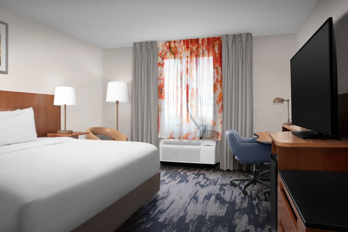 Een hotelkamer met een groot bed, een bureau met een computer, een televisie en een raam met gordijnen.
