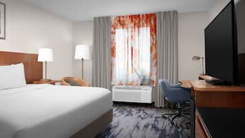Habitación de hotel con una cama grande, un escritorio con computadora, un televisor y un ventanal con cortinas.