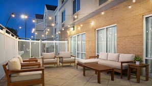 An outdoor patio area with a sofa set, wooden tables, and string lights. - Fairfield Inn & Suites by Marriott at Dulles Airport (Sterling)