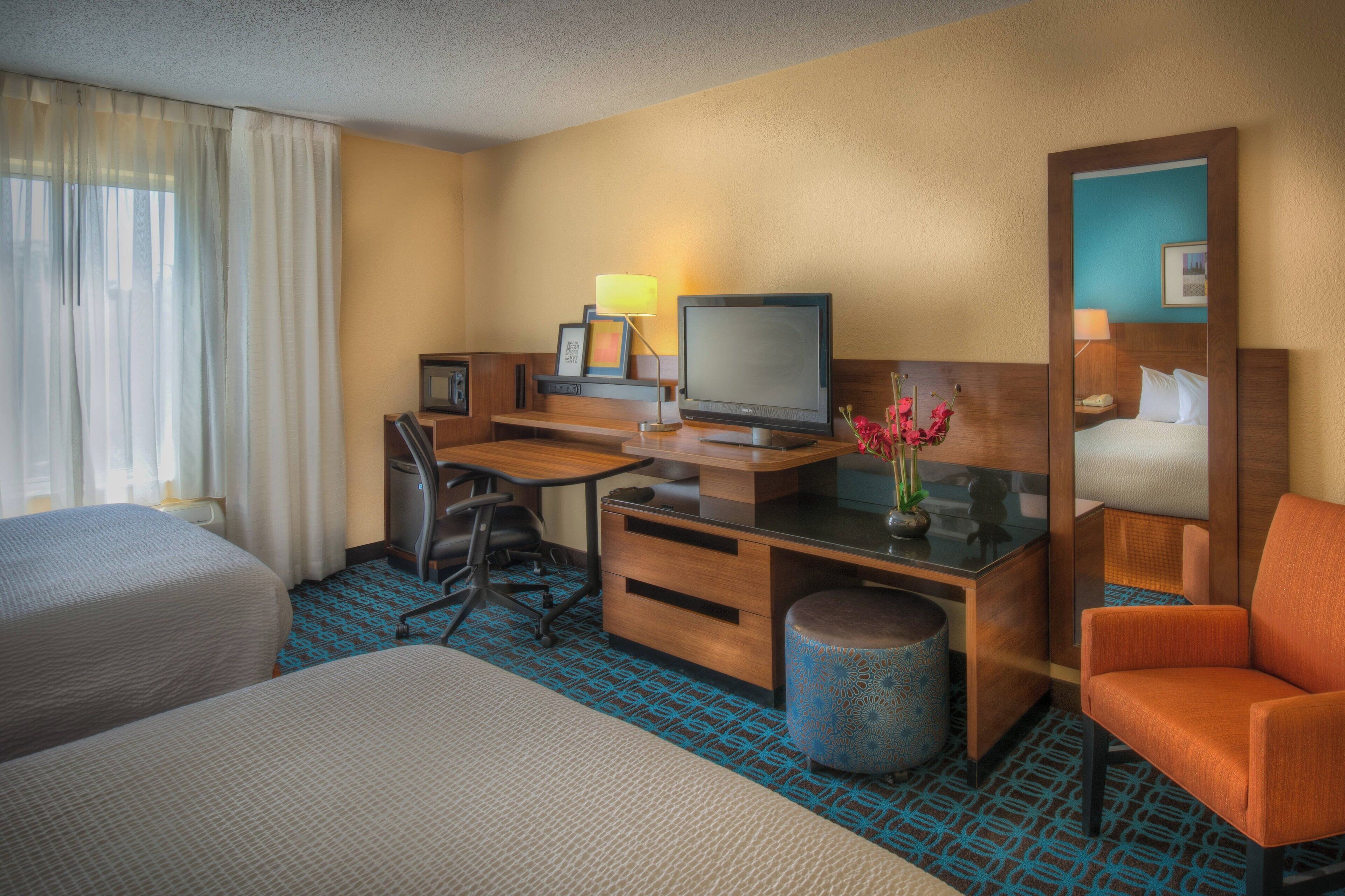 A hotel room with two beds, a desk with a computer, a chair, a lamp, and a small trash can.