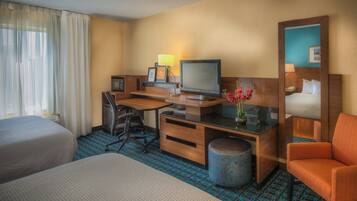A hotel room with two beds, a desk with a computer, a chair, a lamp, and a small trash can.