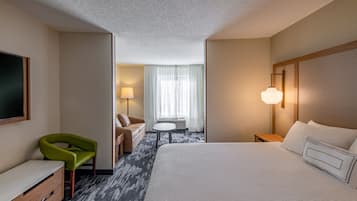 Ein Hotelzimmer mit einem großen Bett, einem grünen Sessel, einem Schreibtisch, einer Lampe und einem Fenster mit Vorhängen.