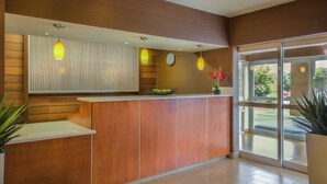 A reception area with a wooden reception desk, a clock, and a large window offering a view of the outdoors.