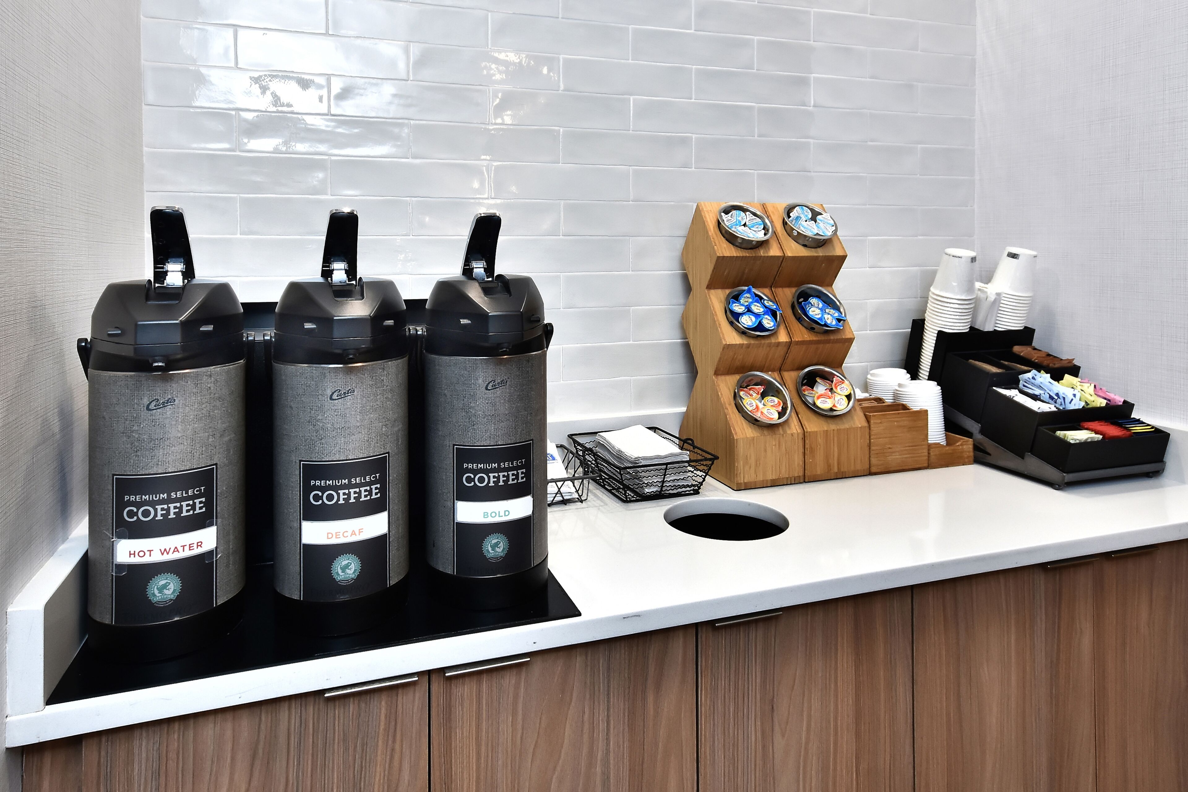 A coffee station with three coffee dispensers, a coffee cup holder, and a variety of coffee cups and napkins.