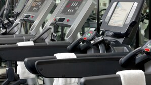 A row of stationary exercise bikes with digital displays, each equipped with a control panel and a towel on the seat.