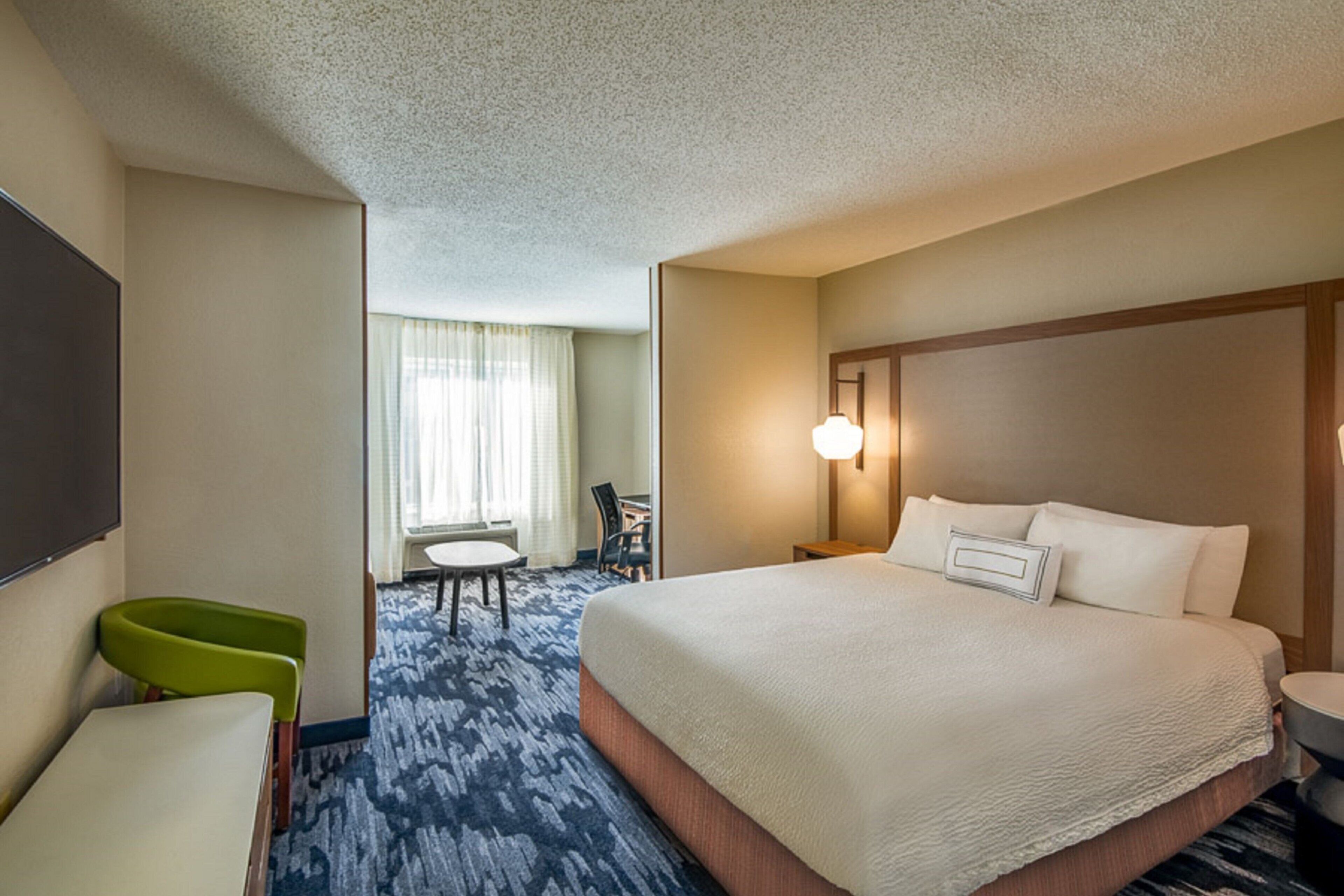 A hotel room with a large bed, a desk, a chair, and a television.