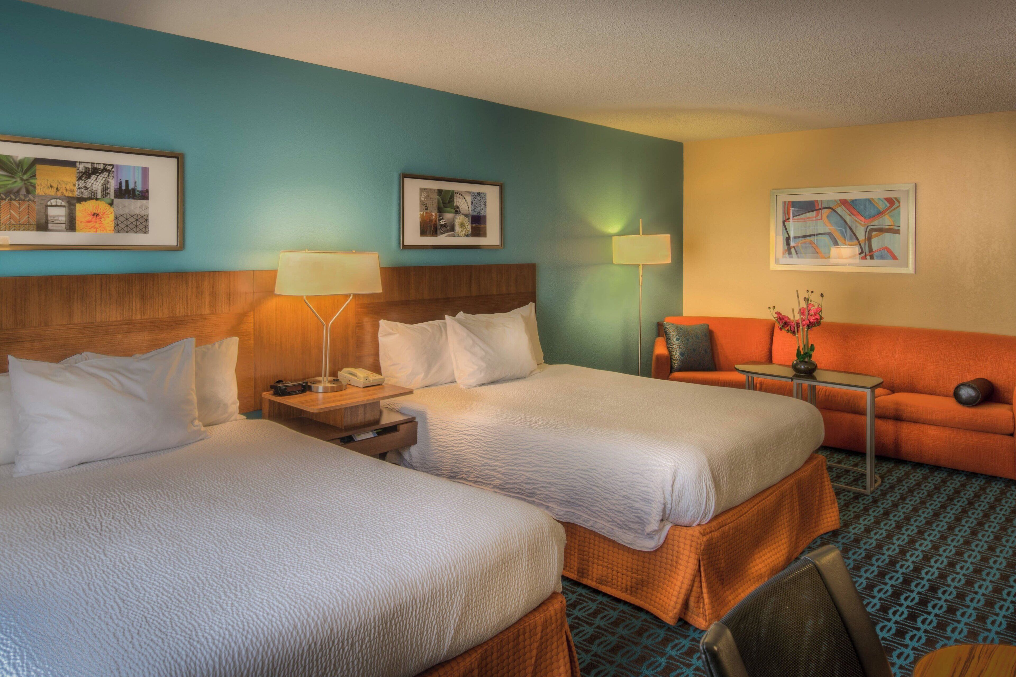 A hotel room with two beds, a sofa, a small table, and a lamp.