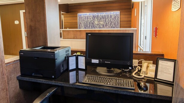 A reception desk with a desktop computer, a printer, a telephone, and a framed sign. - Fairfield Inn By Marriott Potomac Mills (Woodbridge)