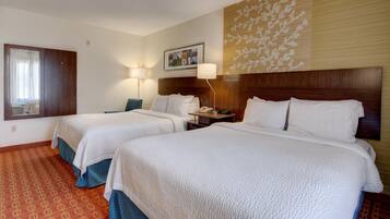 A hotel room with two beds, a wooden headboard, a wall-mounted lamp, a bedside table with a phone, and a patterned carpet.