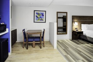 A hotel room with a dining area, a bed, a nightstand, a mirror, and a small kitchen area.