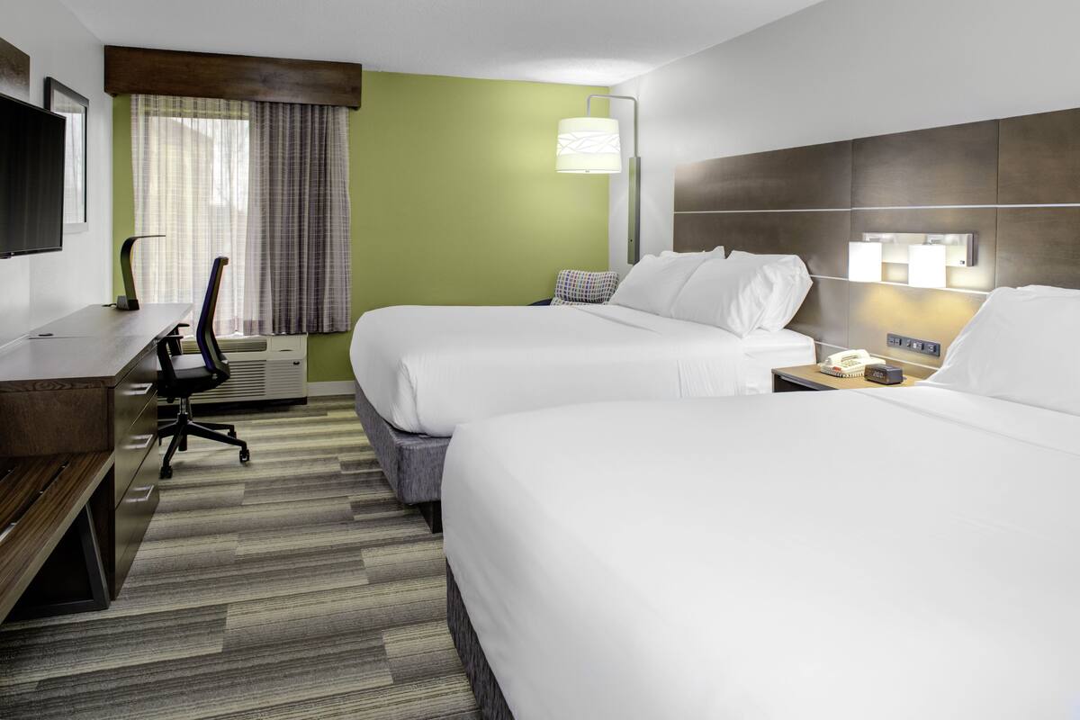 A hotel room with two beds, a desk, a chair, a TV, and a window with curtains.