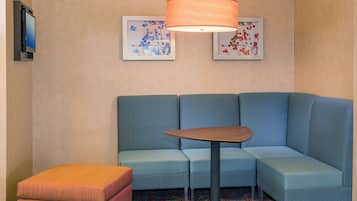 Una habitación de hotel moderna con un sofá modular, una pequeña mesa de madera y una lámpara de pie grande.
