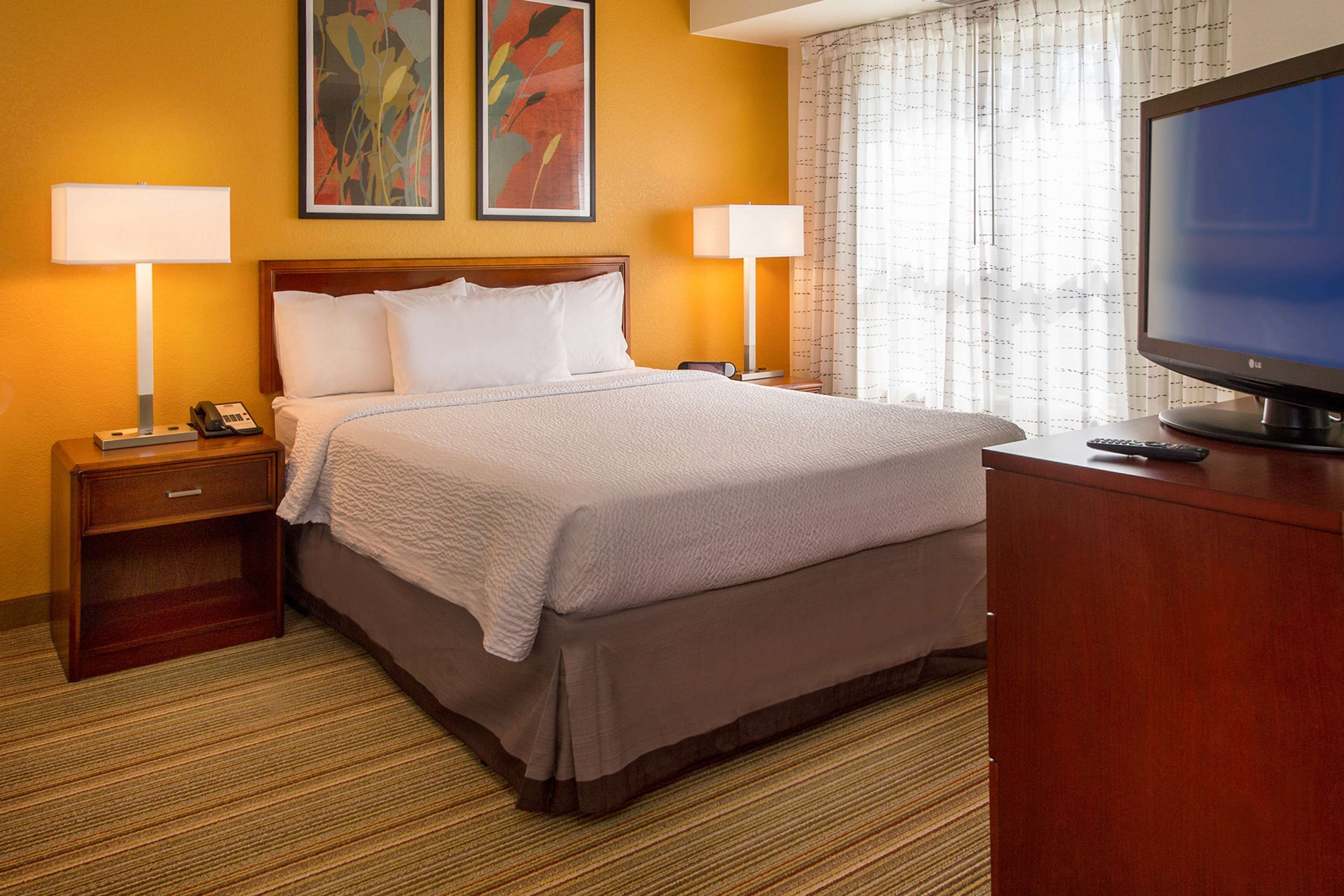 Habitación de hotel con una cama grande, dos lámparas de noche, una televisión y una mesita de noche con un teléfono.