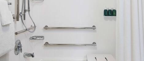 Une salle de bain moderne dotée d’une douche à l’italienne, de barres d’appui, d’une baignoire et d’un porte-serviettes.