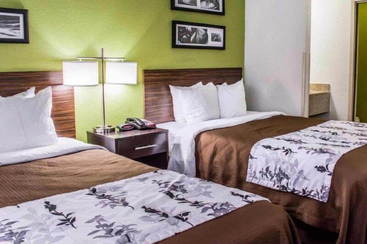 A hotel room with two beds, a nightstand, a lamp, and framed pictures on the wall.