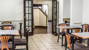 Un espace repas avec des tables et des chaises, un sol carrelé et un escalier menant à une autre pièce.