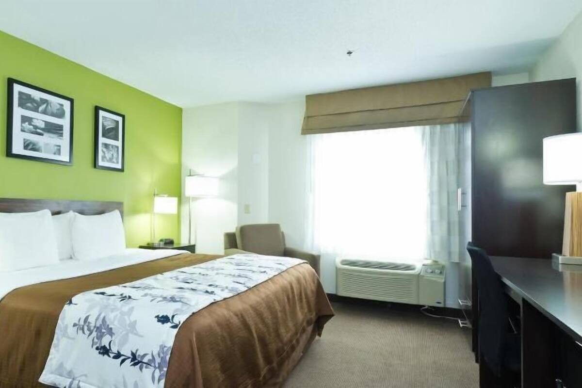 A hotel room with a bed, a desk, a chair, a TV, and a window with curtains.